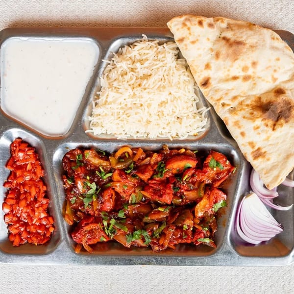 A metal tray with sections of rice, naan, chicken chili, yogurt, chopped tomatoes, and red onion.