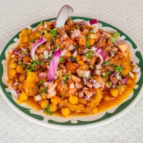 A vibrant plate of Indian chaat, topped with chickpeas, diced tomatoes, red onions, and cilantro.