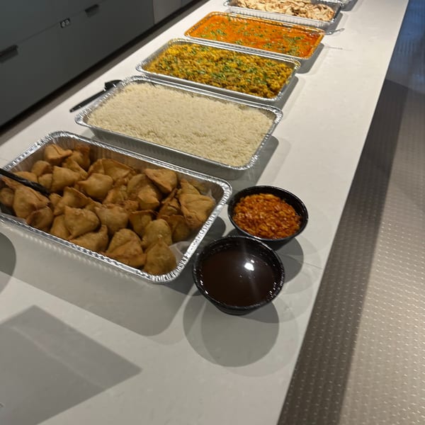 A buffet line of Indian food, including samosas, rice, curries, and naan bread.