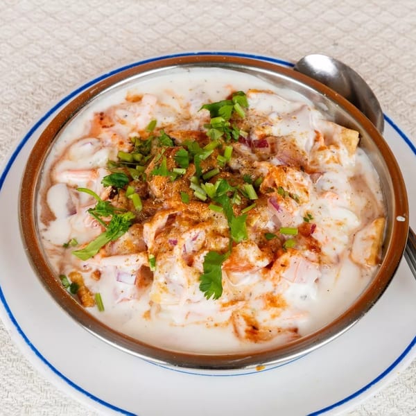 Close-up of a bowl of dahi vada, topped with red onions, spices, and fresh cilantro.