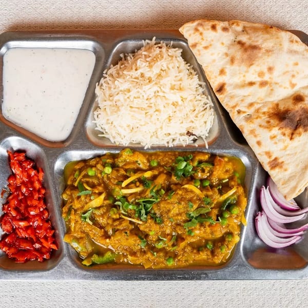 Indian thali with curry, rice, naan, raita, pickled vegetables, and red onion slices.