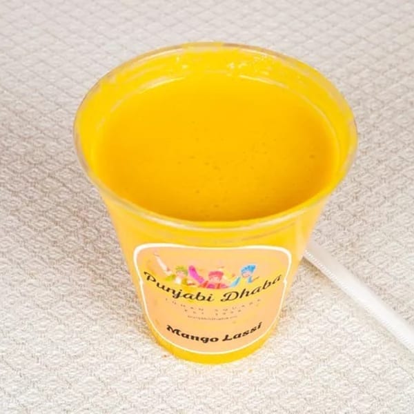 A yellow cup of mango lassi from Punjabi Dhaba with a white straw on a textured white surface.