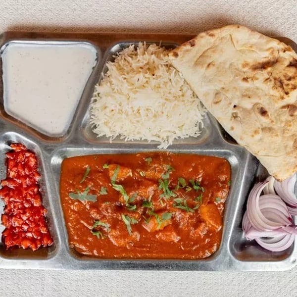 Indian thali with butter chicken, rice, naan, yogurt, pickled vegetables, and sliced onions.